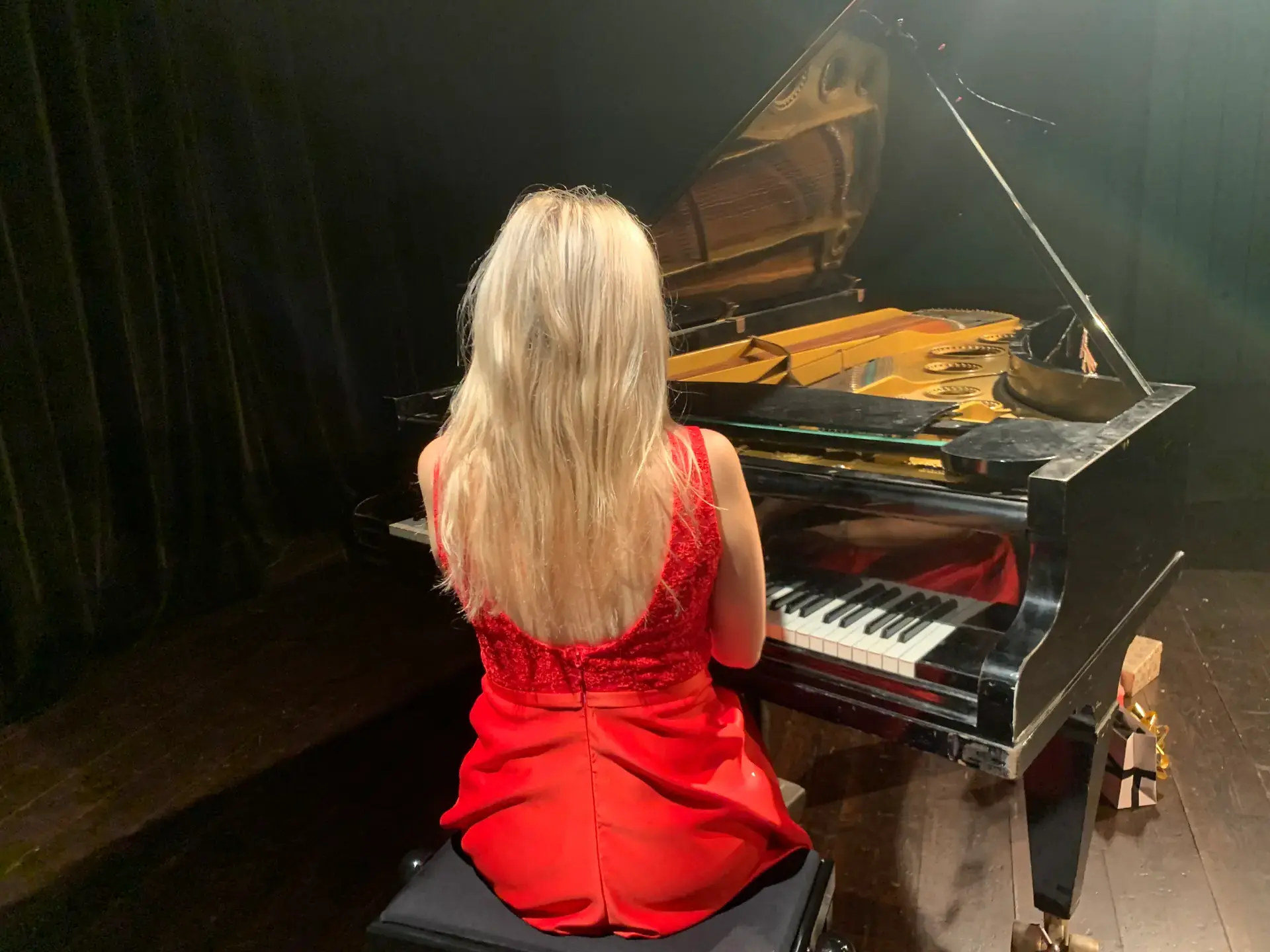 Maria Millini vid flygel i röd klänning