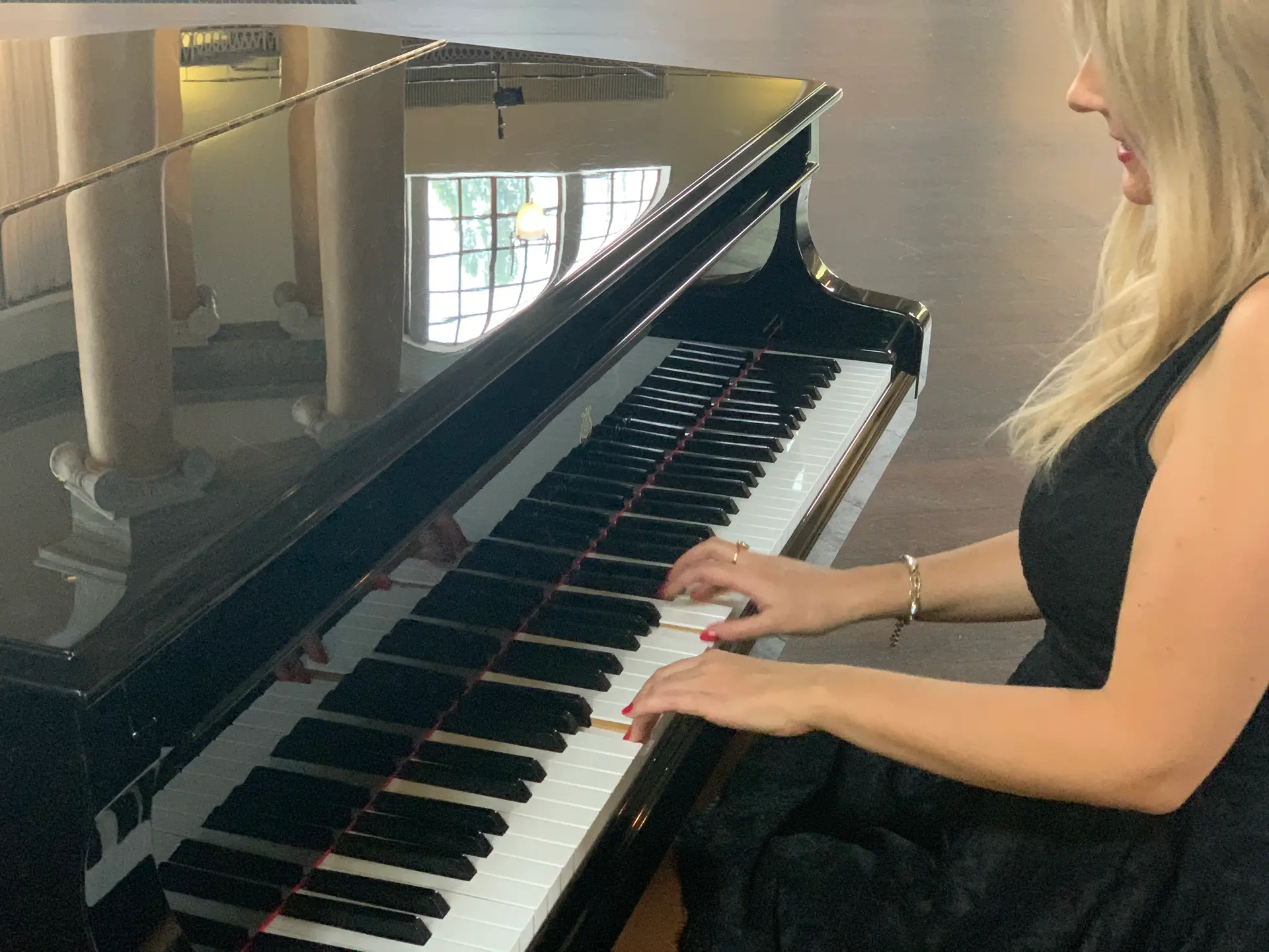 Maria Millini vid piano i elegant svart klänning